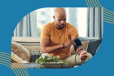 Black man in an orange shirt taking his blood pressure at home using a blood pressure cuff