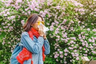 Young person sneezes among blooming trees.