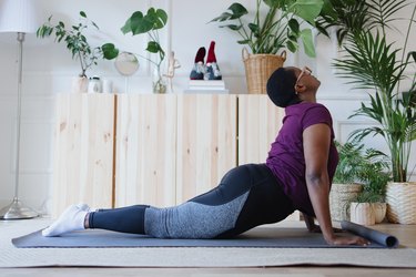 Person practicing upward dog as part of sun salutation on yoga mat in living room