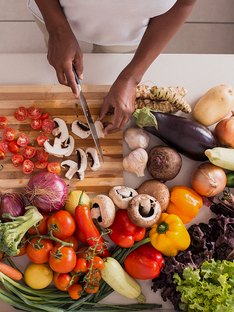 Woman on a weight-loss diet chopping a variety of vegetables in her kitchen