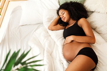 Close up of pregnant person sleeping on their side on a bed with white sheets and blankets