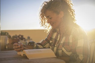 a smiling person with curly blonde hair sitting outside on her terrace at sunset and reading a book, as a nighttime habit for brain health