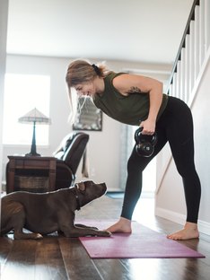 woman strength training with a kettlebell at home with her dog