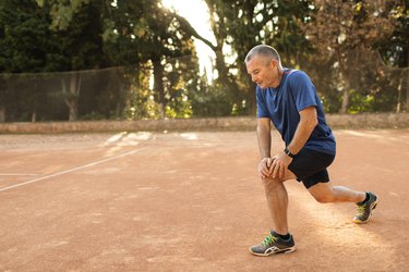 Concentrated senior man warming up and exercising on tennis court. Active lifestyle of old people