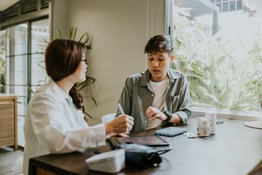 a doctor discussing treatment options with a patient to manage symptoms of medical menopause at a large wooden table in front of a window