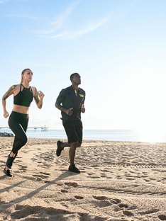 man and woman running on the beach with blue sky