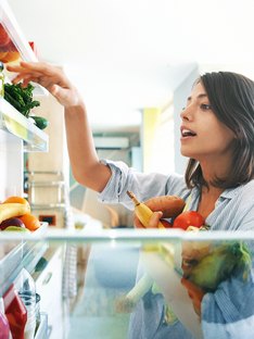 Woman picks out a handful of fruits and veggies from the fridge